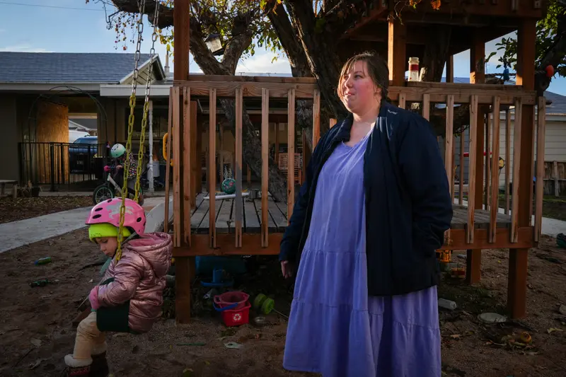 A woman stands behind a child on a swing.